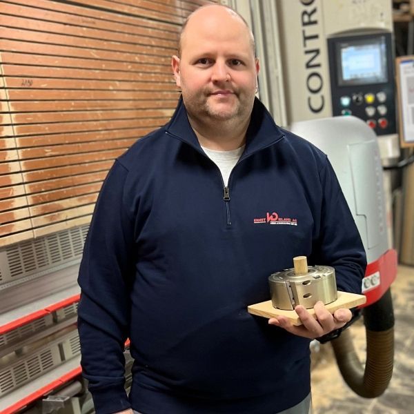 Ein Mann im blauen Hemd hält einen Metallgegenstand vor eine Kontrollmaschine