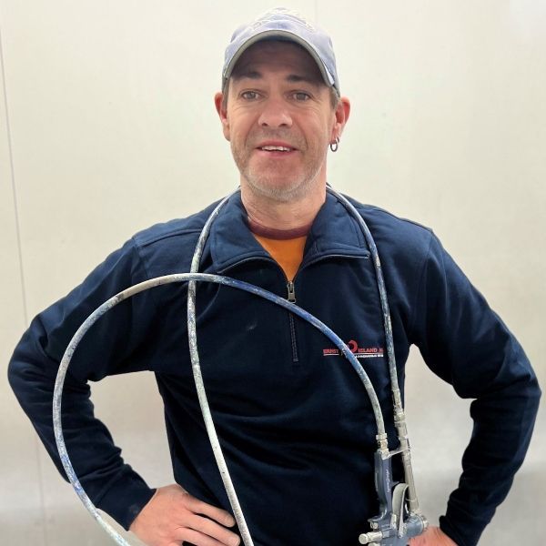 Ein Mann mit Hut und blauer Jacke hält einen Schlauch um den Hals