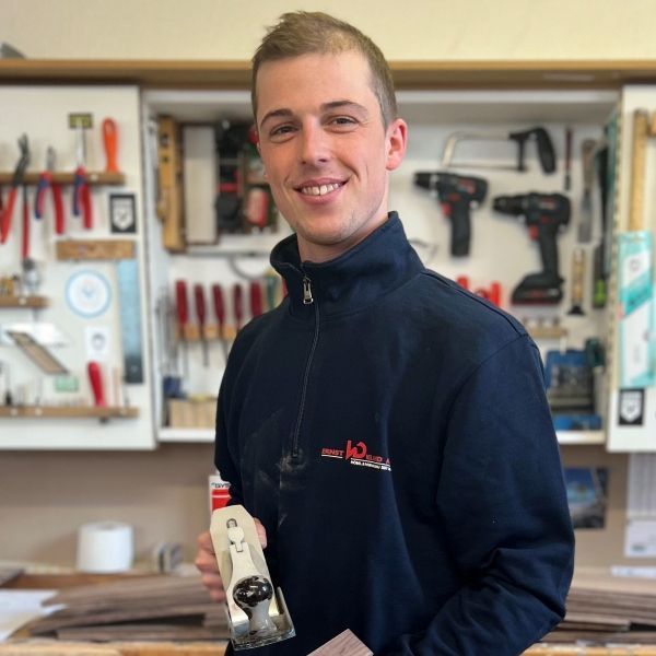 Ein Mann in einer blauen Jacke hält ein Flugzeug und lächelt