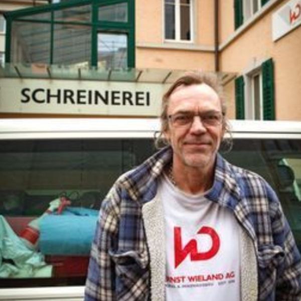 Ein Mann steht vor einem Schild mit der Aufschrift „Schrinerei“