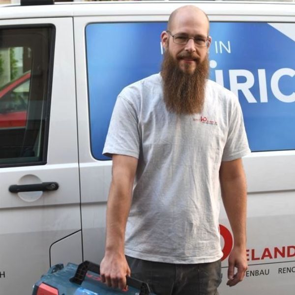 Ein Mann mit Bart steht vor einem Lieferwagen mit der Aufschrift „Ric“