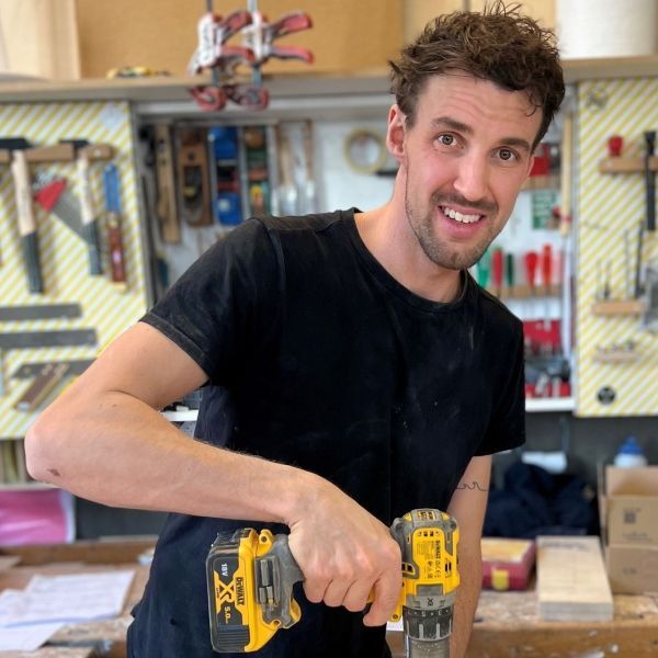 Ein Mann in einem schwarzen Hemd hält eine Bohrmaschine und lächelt