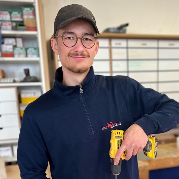 Ein Mann mit Brille und Hut hält eine gelbe Bohrmaschine