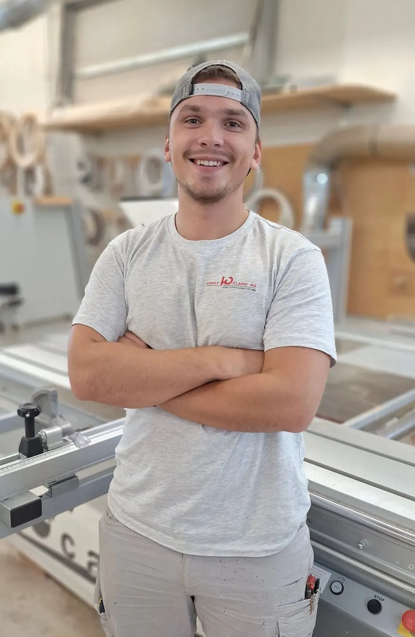 Ein Mann steht mit verschränkten Armen vor einer Maschine und lächelt.