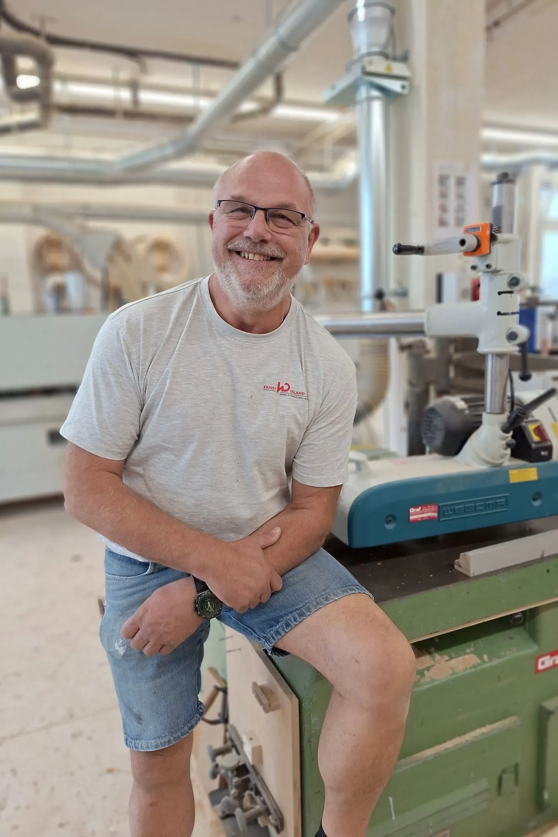 Ein Mann mit Bart sitzt in einer Fabrik auf einer Maschine.