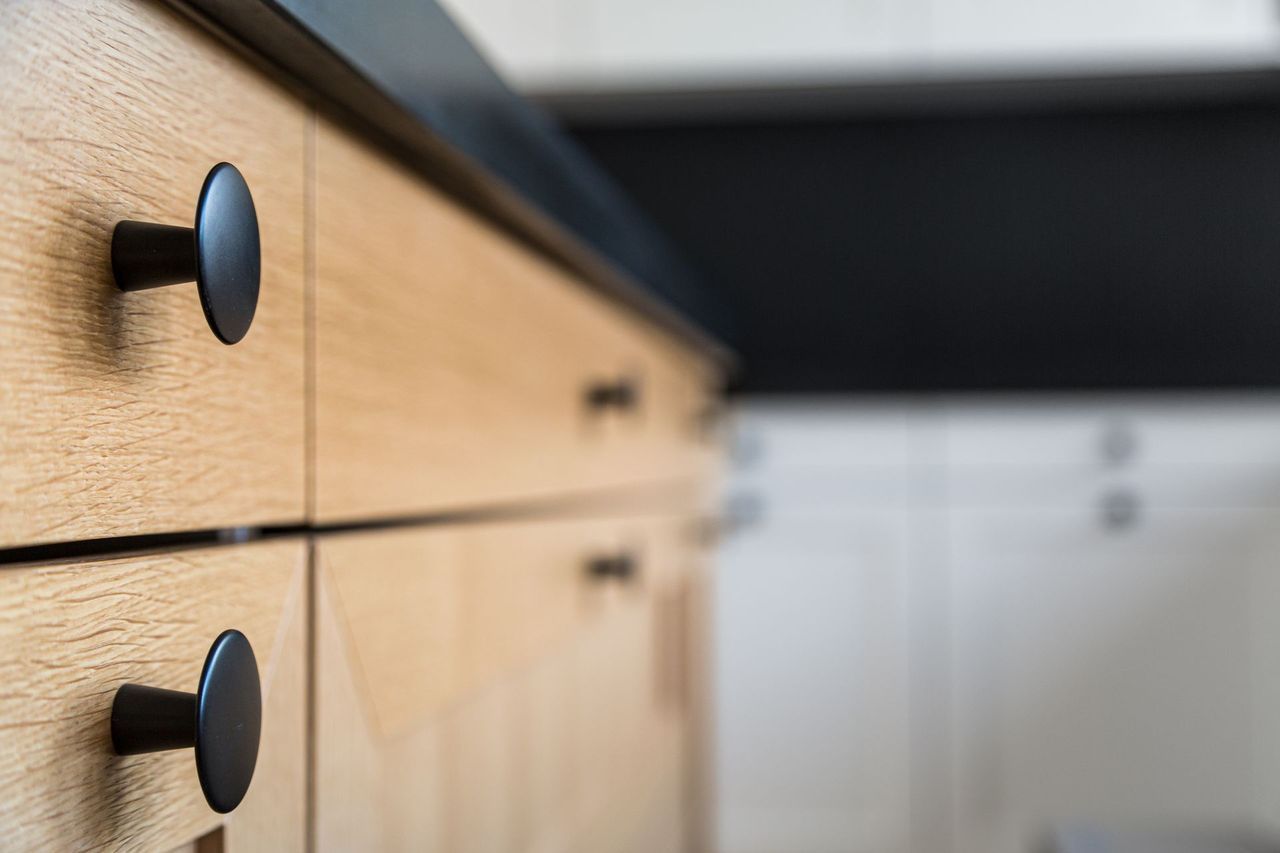 Eine Nahaufnahme eines Holzschranks mit schwarzen Griffen in einer Küche.