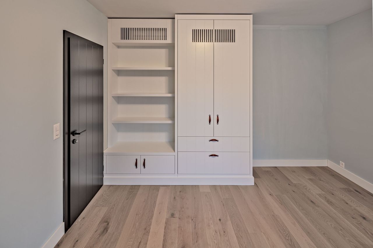 Ein leerer Raum mit einem Kleiderschrank, Regalen, Schubladen und einer Tür.