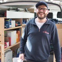 Ein Mann mit Bart und Brille steht hinten in einem Lieferwagen.