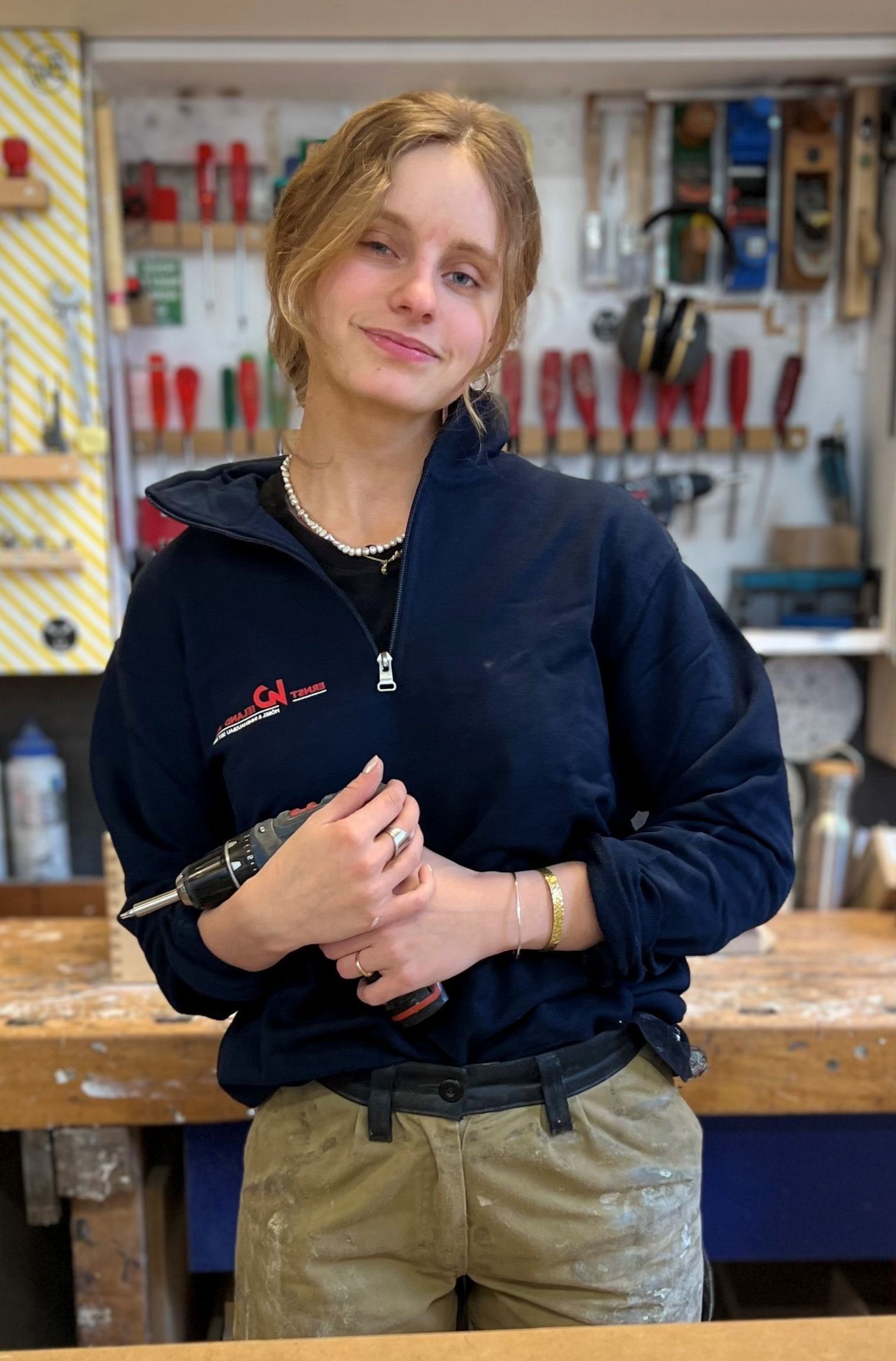 Eine junge Frau steht mit einer Bohrmaschine in einer Werkstatt.