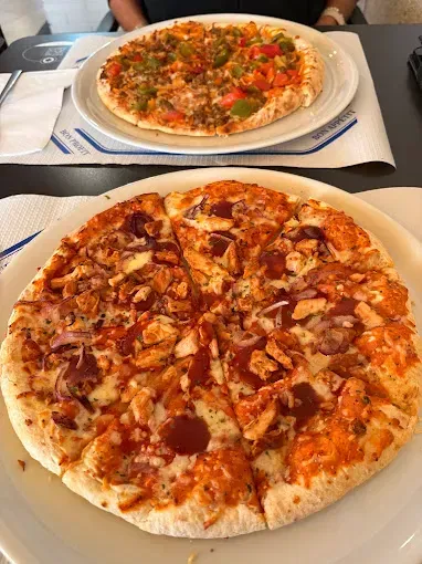 Hay dos pizzas en platos sobre una mesa.