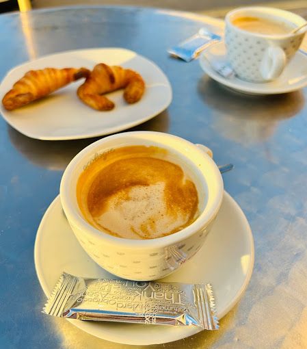 Una taza de café reposa sobre un platillo en una mesa junto a un plato de croissants.