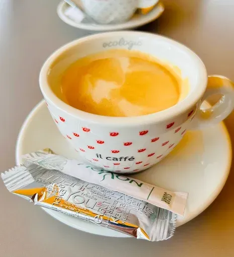 Una taza de café reposa en un platillo junto a un paquete de azúcar.