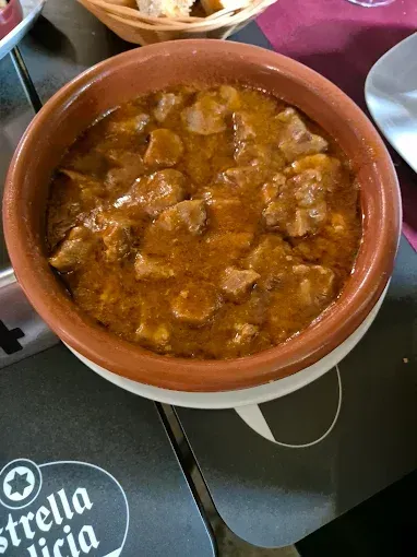 Un plato de estofado reposa sobre una mesa junto a un cartel que dice Estrella Galicia.