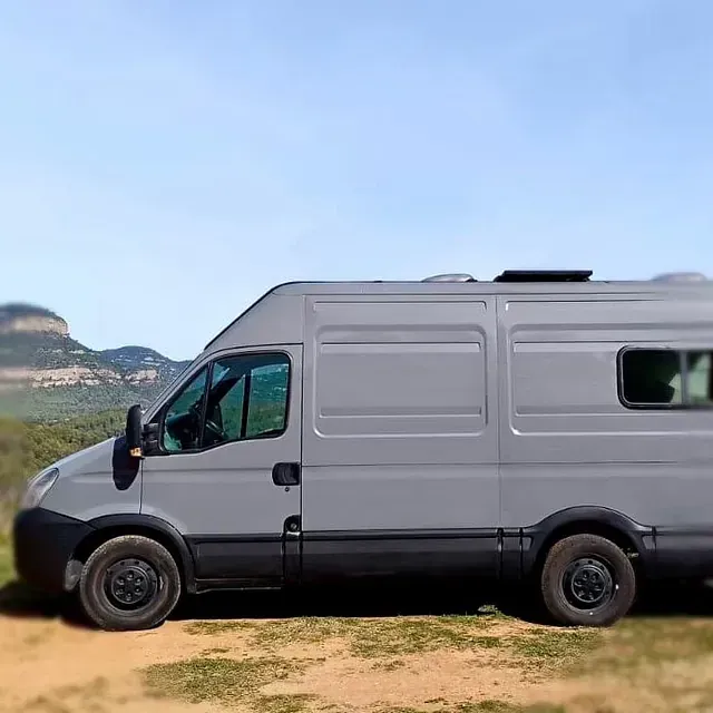Autocaravana gris estacionada en un camino de tierra con un fondo de montañas.