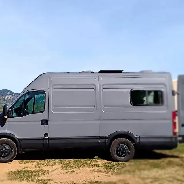 Una autocaravana gris estacionada al aire libre en un día soleado. Se ven neumáticos negros, una ventana oscura y la ventilación del techo.