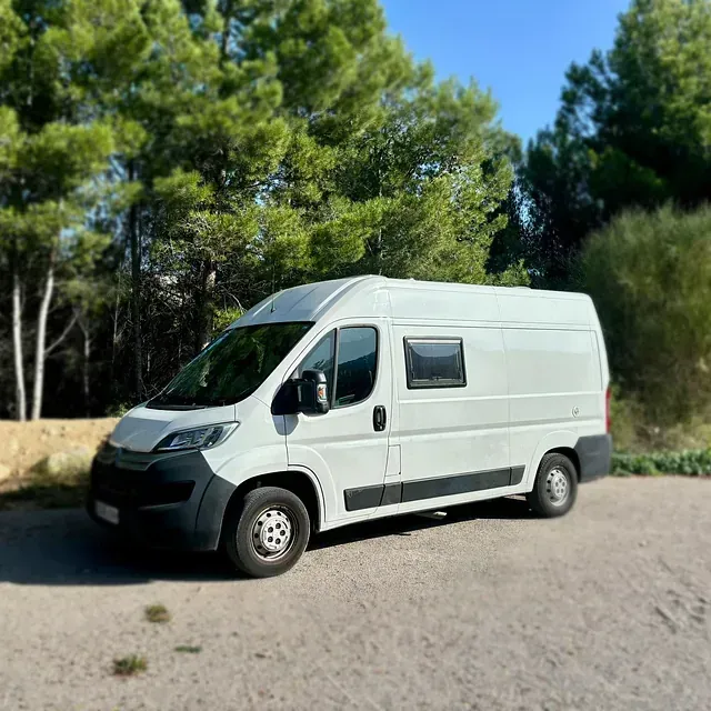 Autocaravana blanca estacionada en una carretera asfaltada con árboles al fondo en un día soleado.