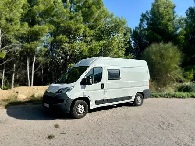 Autocaravana blanca estacionada en un camino de grava en una zona boscosa.