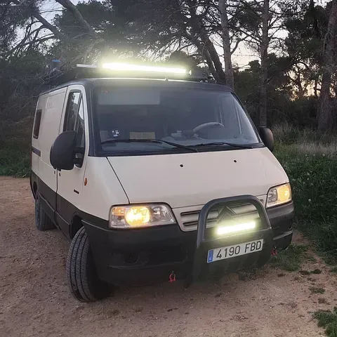 Furgoneta camper de color beige y negro con barras de luz en un camino de tierra.