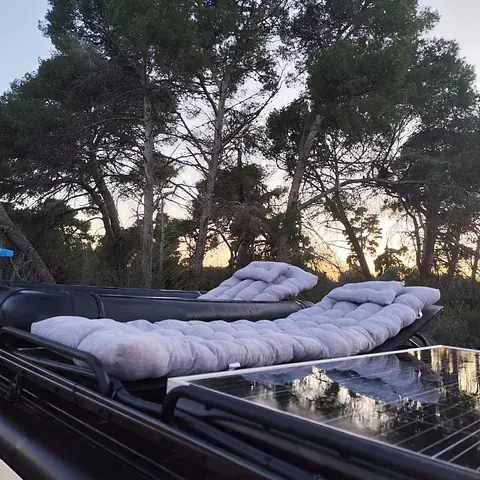 Dos sillones con cojines grises en la cubierta de un barco con árboles de fondo al anochecer.
