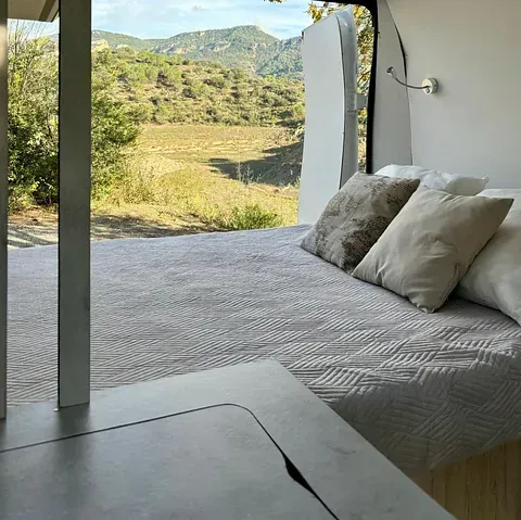 Dentro de una autocaravana, una cama con almohadas mira hacia la montaña.