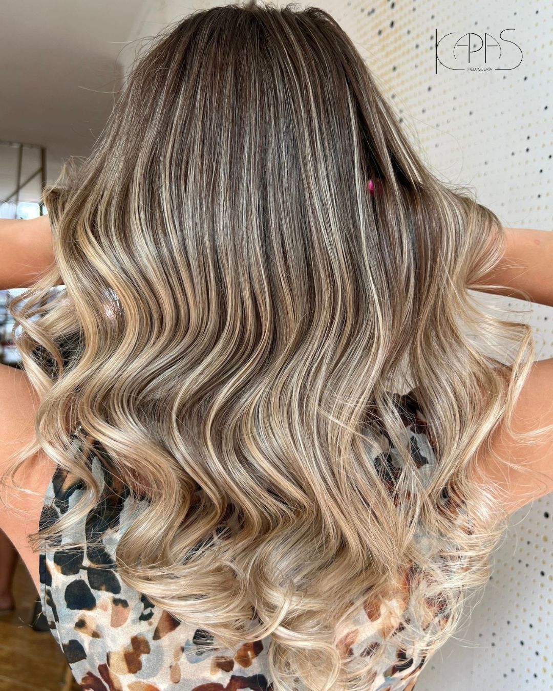 Cabello largo y ondulado con mechas balayage rubias y castañas, peinado hacia abajo, visto desde atrás.