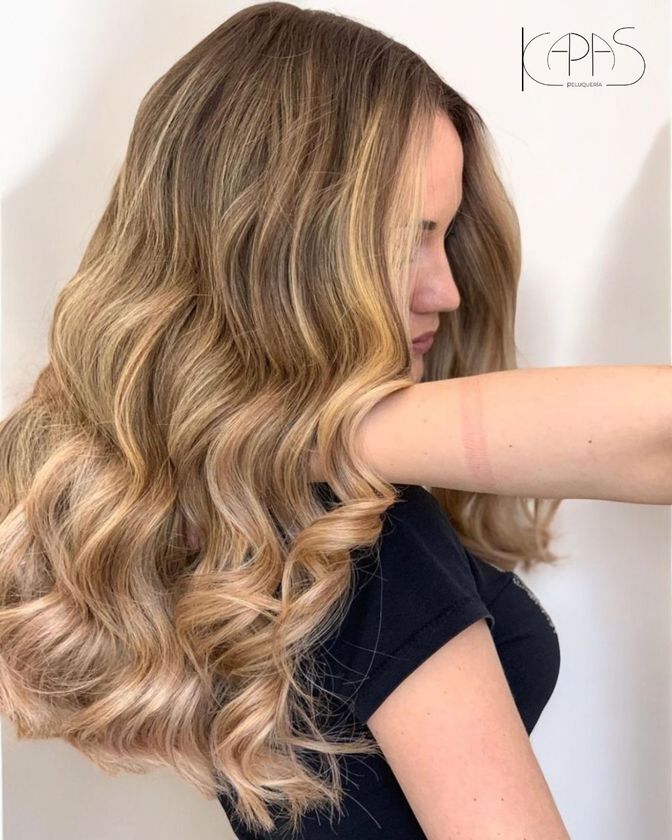 Perfil de una mujer con cabello rubio largo y ondulado, mostrando suaves rizos sobre un fondo blanco.