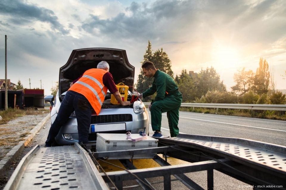 Zwei Fachleute arbeiten bei Sonnenuntergang an Auto auf Anhänger Straßenrand.