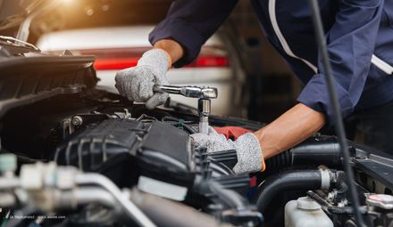 Mechaniker mit Handschuhen nutzt Ratsche am Motor unter offener Motorhaube