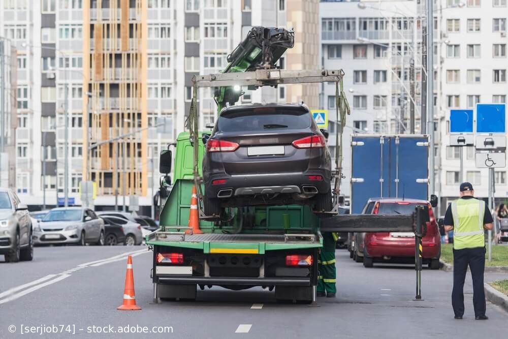 Ein Abschleppwagenfahrer verlädt auf einer Straße in der Stadt einen dunklen Geländewagen auf einen Tieflader.