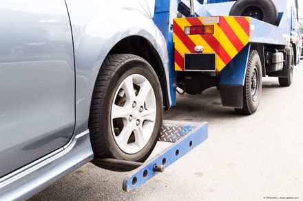 Graues Auto von blauem Abschleppwagen gezogen, Vorderreifen in Hebevorrichtung gesichert