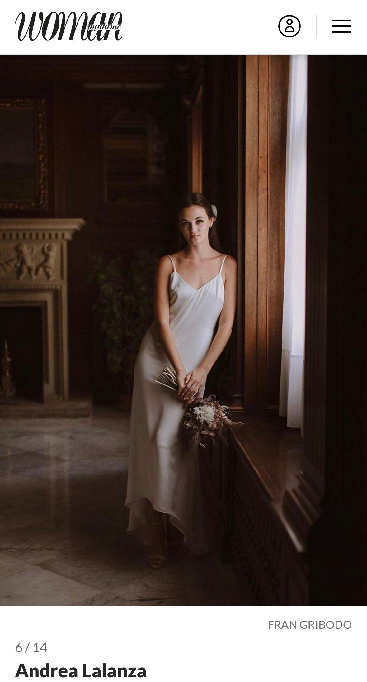 Una mujer con un vestido blanco está de pie junto a una ventana sosteniendo un ramo de flores.