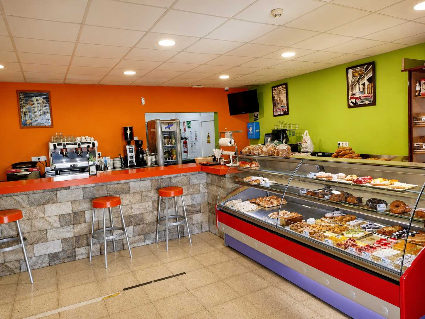 Barra de cafetería luminosa con taburetes, vitrina para pasteles y paredes de color naranja y verde lima.