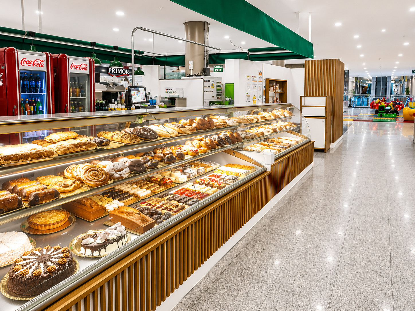 Vitrina de panadería con pasteles y tartas variadas en un pasillo luminoso de un supermercado.