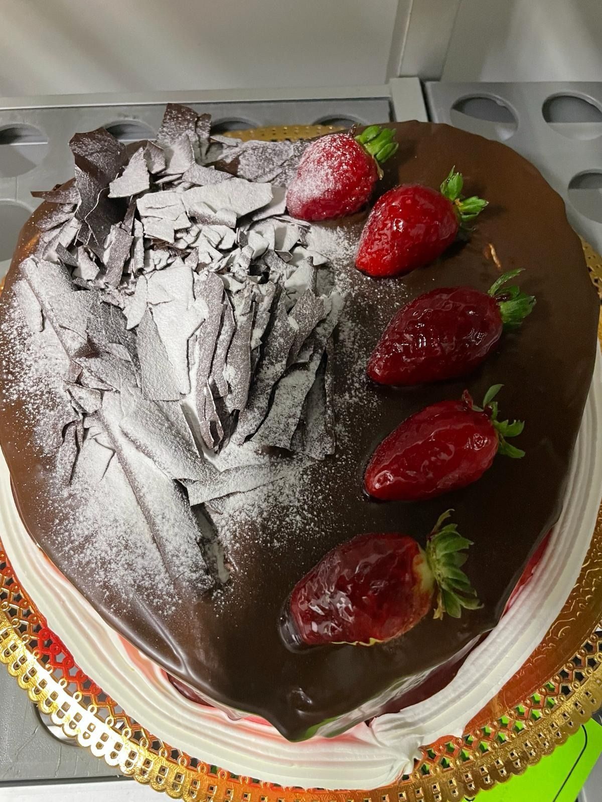Pastel de chocolate cubierto con azúcar glas y fresas frescas sobre una base dorada para pasteles.