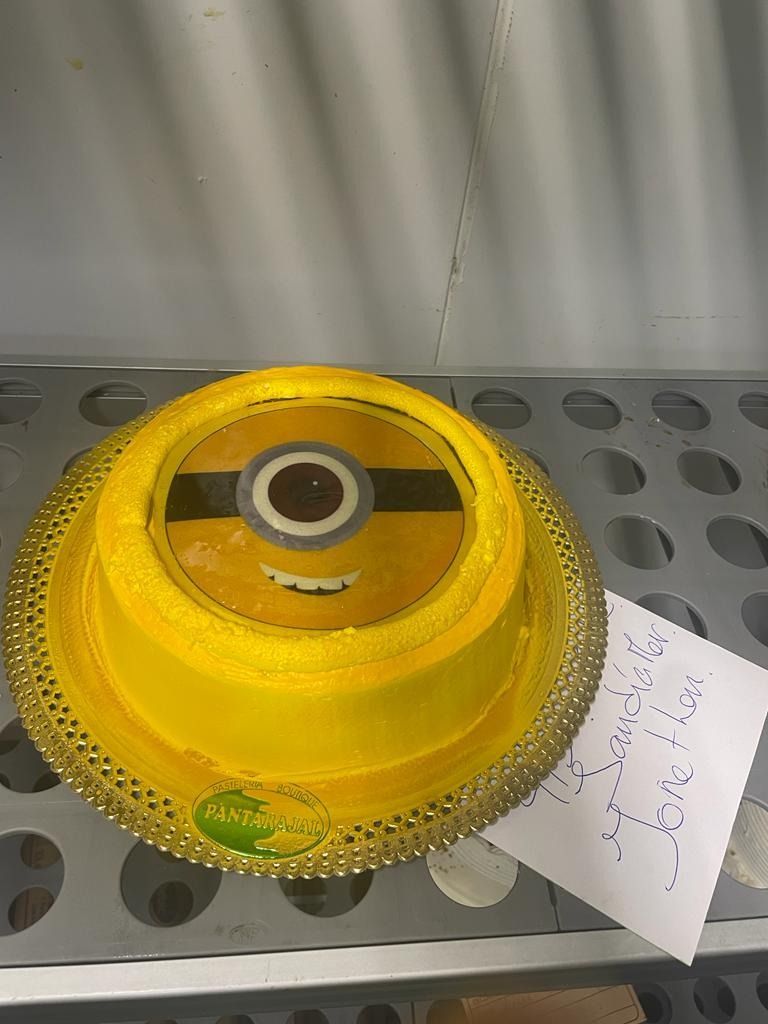 Pieza industrial amarilla sobre una estantería metálica perforada con una nota escrita a mano adjunta.