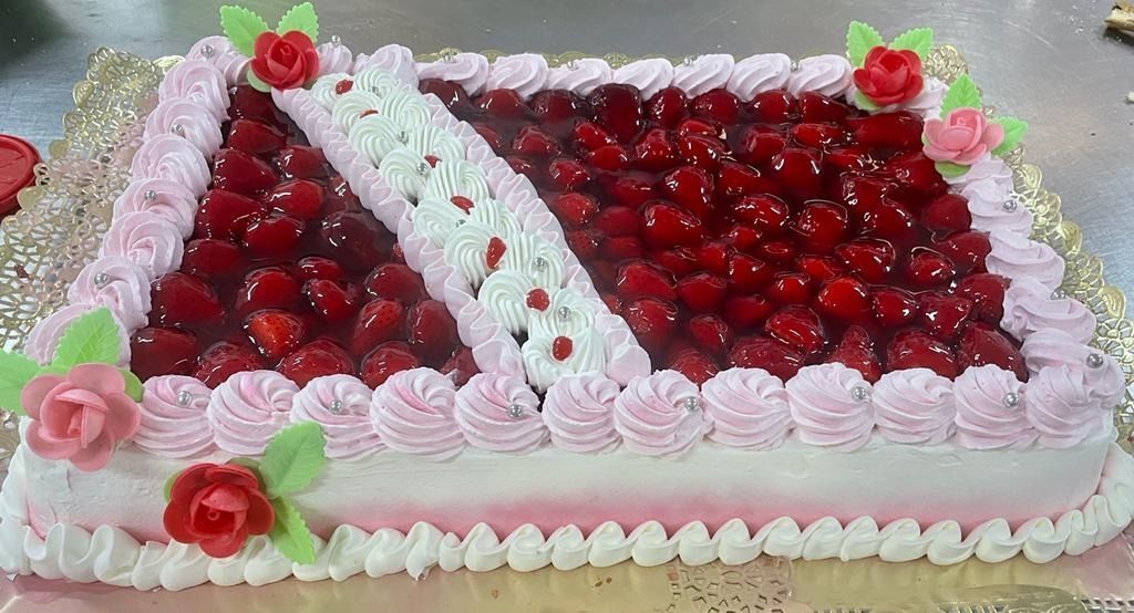 Tarta rectangular decorada con glaseado blanco y cobertura de fruta roja, adornada con rosas rosadas.