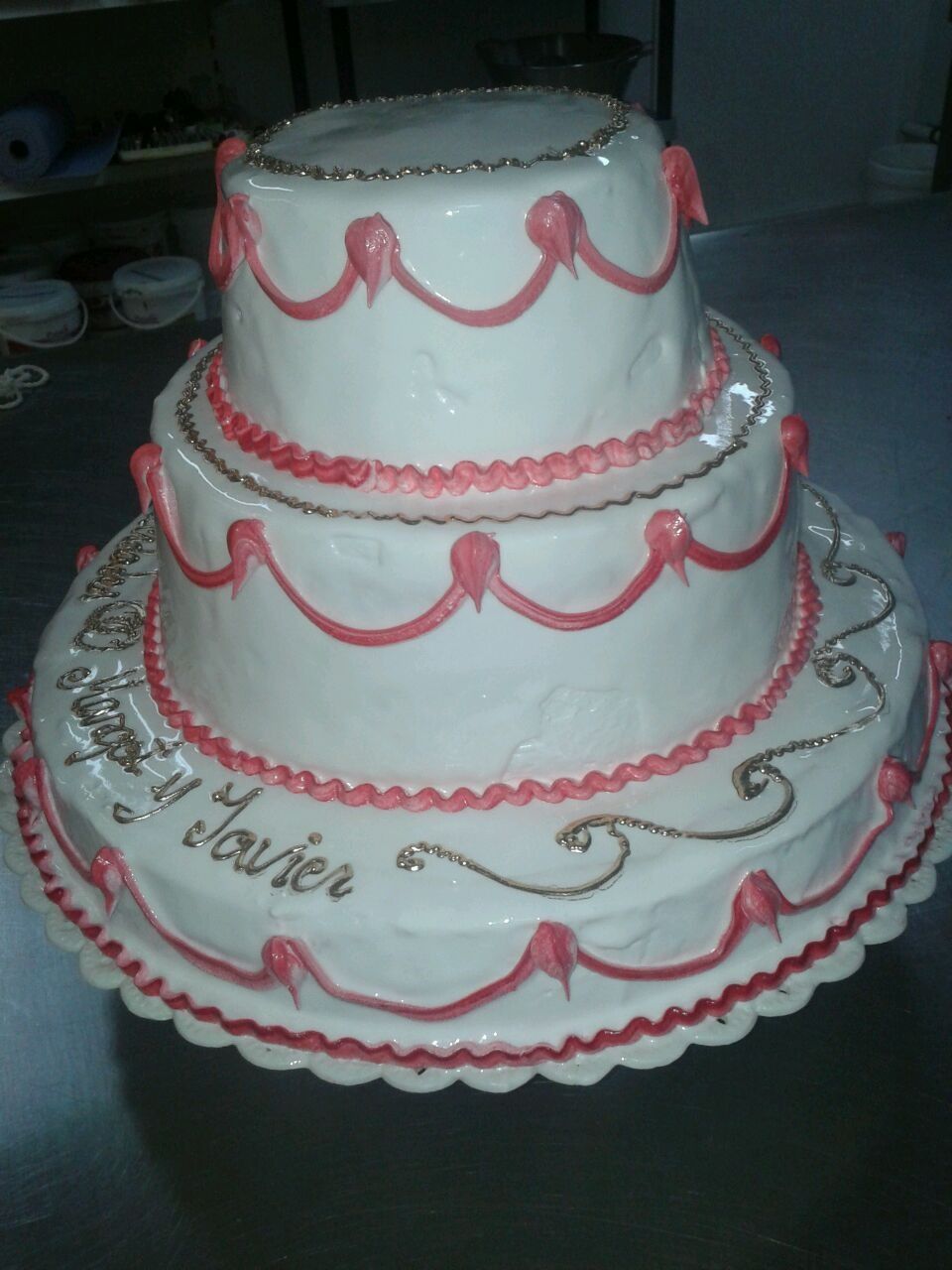 Tarta de boda blanca de tres pisos con ribete rosa y plateado sobre una base festoneada.