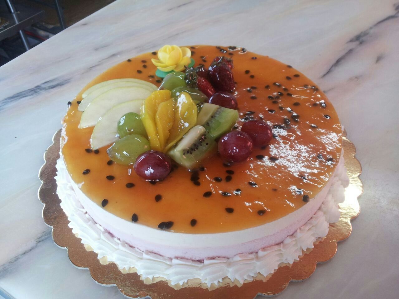 Pastel redondo con frutas y glaseado de naranja sobre una base dorada.
