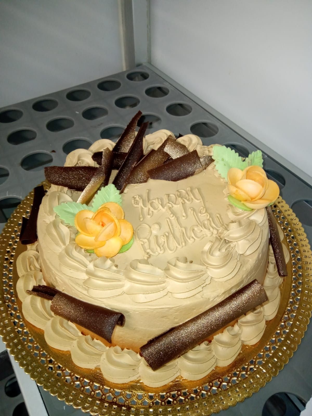 Tarta de crema decorada con barquillos de chocolate y flores amarillas sobre una base dorada.