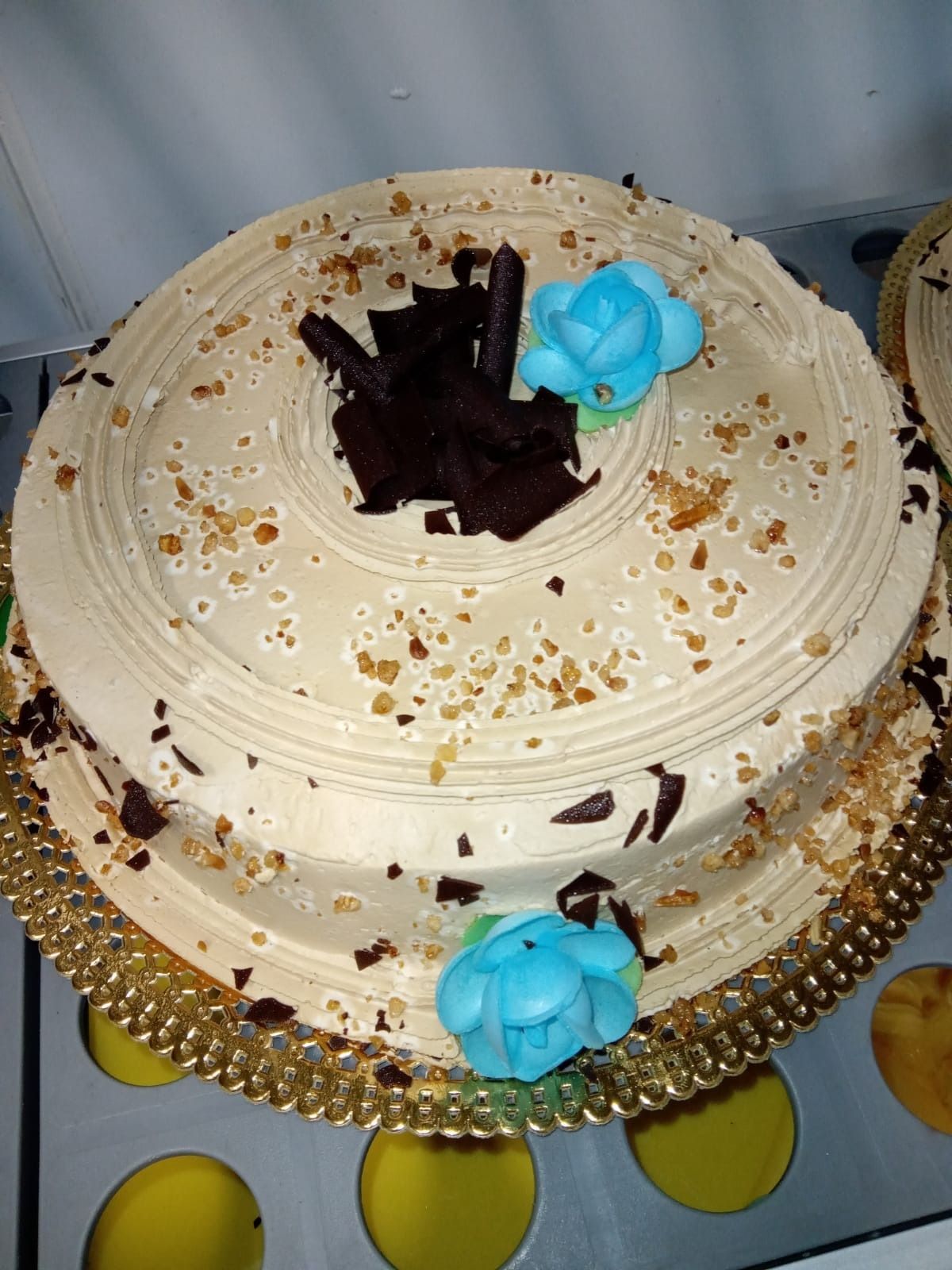 Pastel redondo blanco glaseado con centro de chocolate negro y flores azules sobre una bandeja dorada.