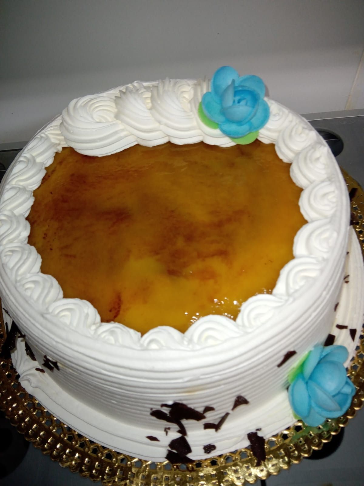 Pastel blanco glaseado con glaseado de caramelo y decoración de flores azules sobre una base dorada.