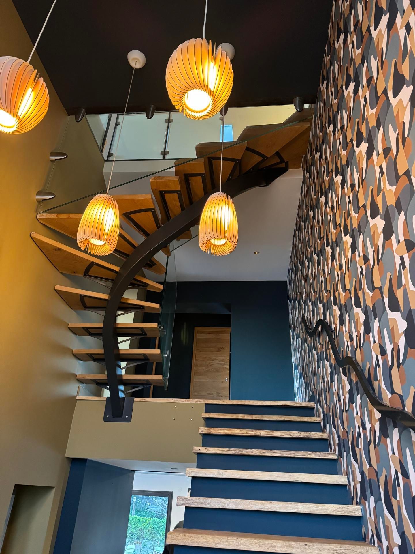 Escalier en colimaçon dans un intérieur moderne avec des suspensions lumineuses à lumière chaude et des panneaux muraux à motifs