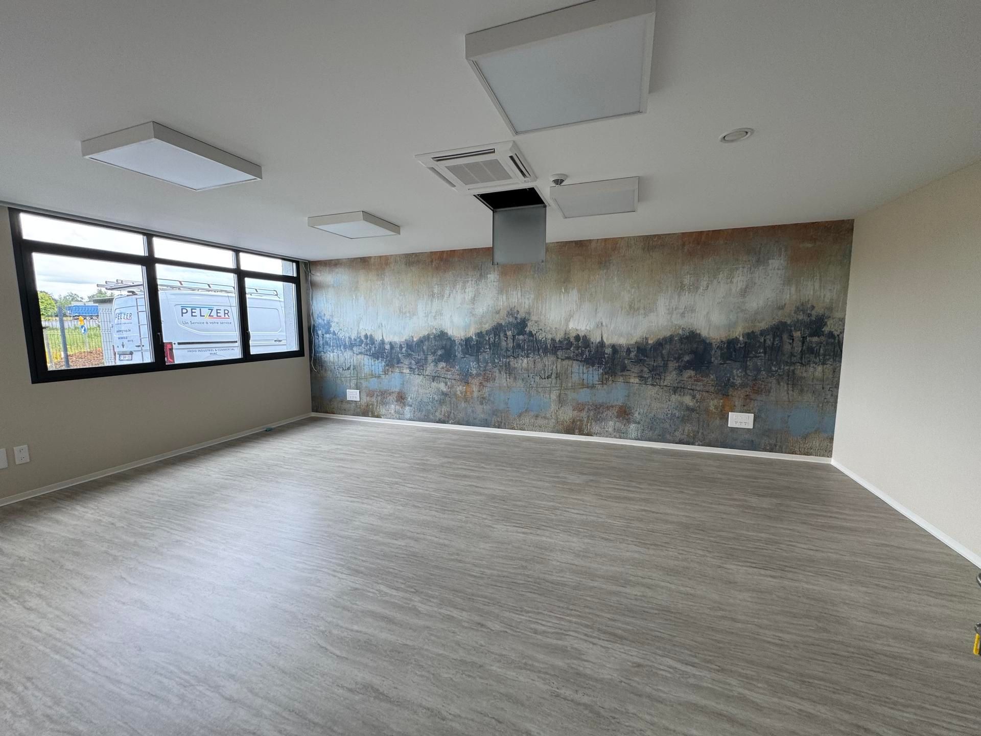 Bureau moderne vide avec fenêtres, sol gris, éclairage au plafond et une grande fresque murale texturée