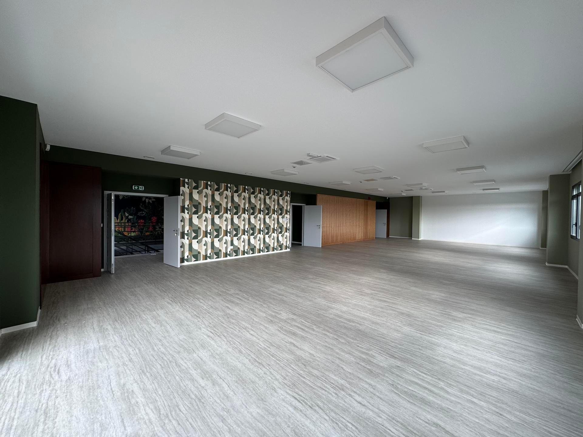 Pièce moderne vide avec moquette grise, luminaires blancs au plafond et cloison murale à motifs.