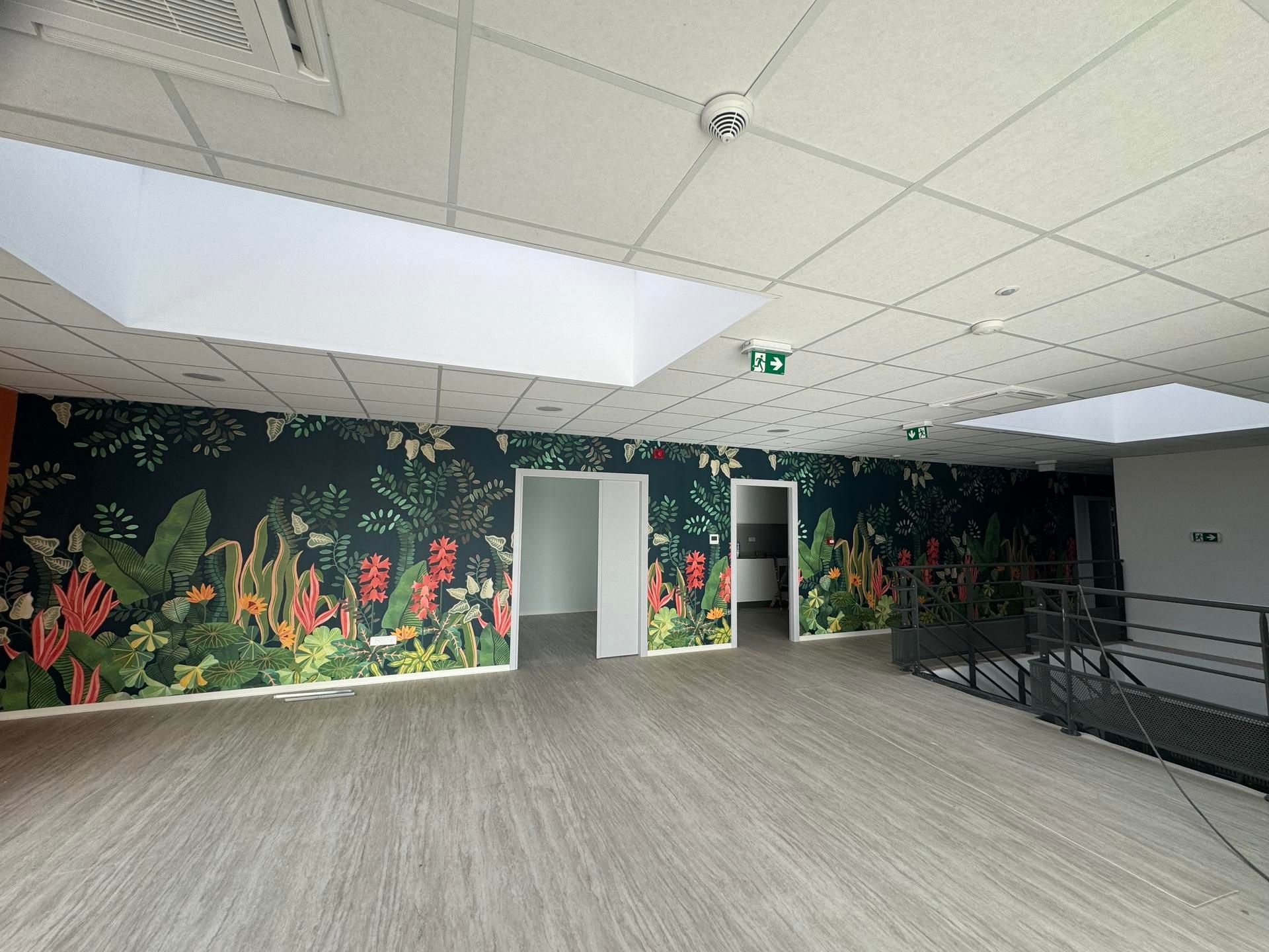 Hall d'entrée intérieur vide avec fresque florale, moquette grise, panneaux de plafond blancs et rampe d'escalier.