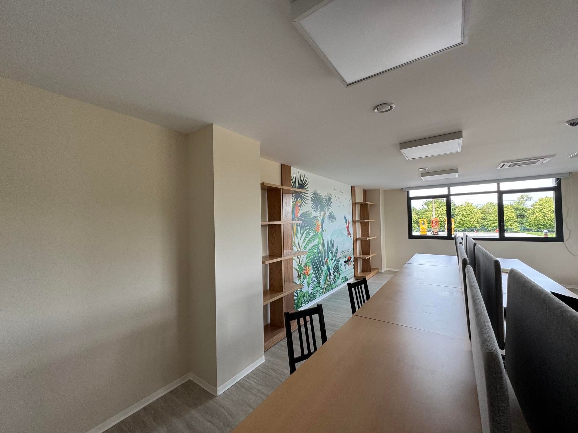 Couloir lumineux avec un long bureau en bois, des étagères intégrées et de grandes fenêtres dans une pièce moderne