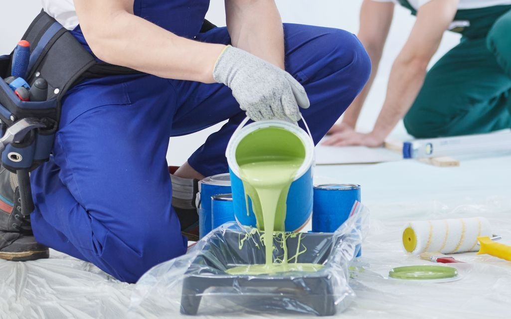 un homme qui verse de la peinture verte dans un bac