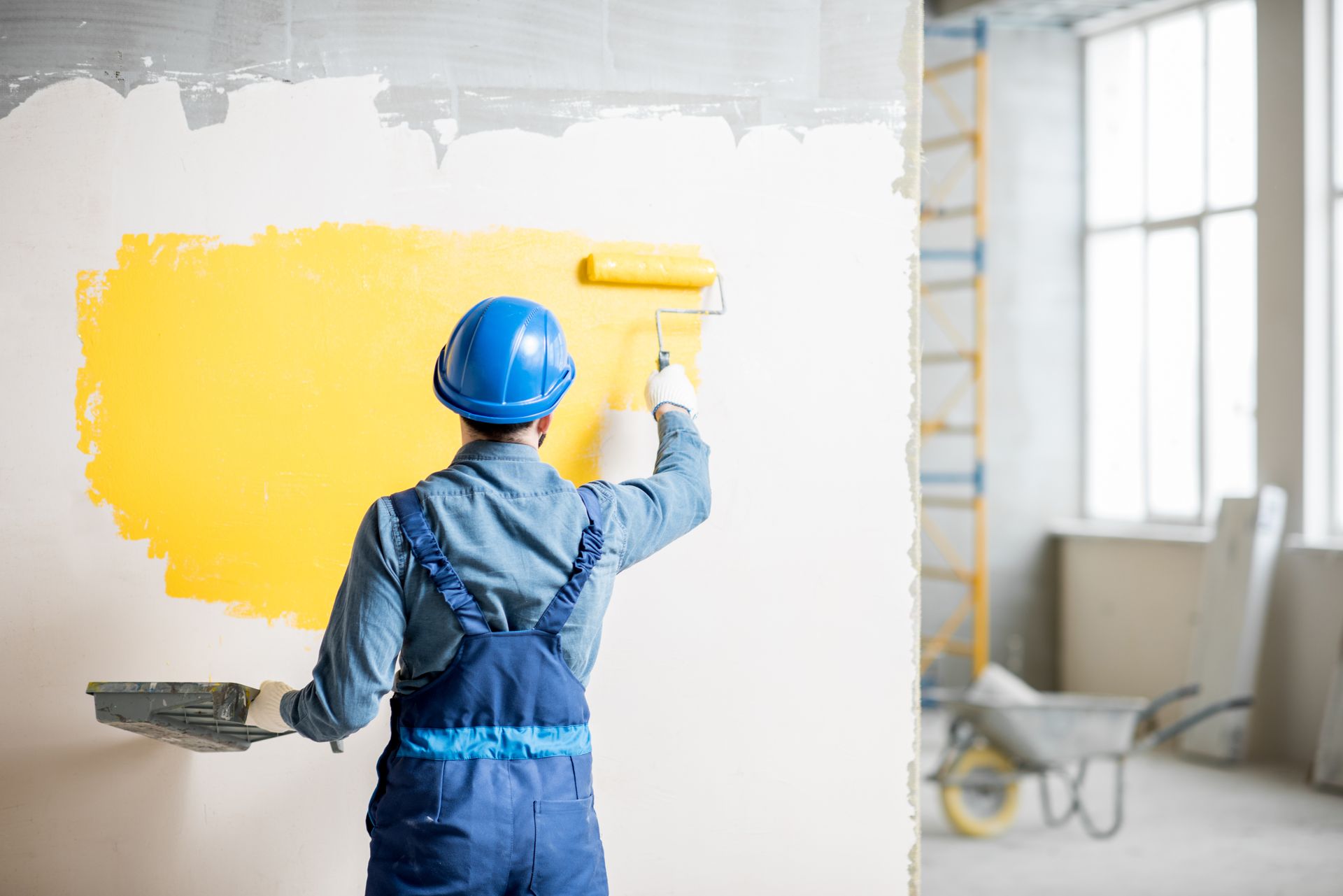 Homme qui peint un mur avec un rouleau et une peinture de couleur jaune
