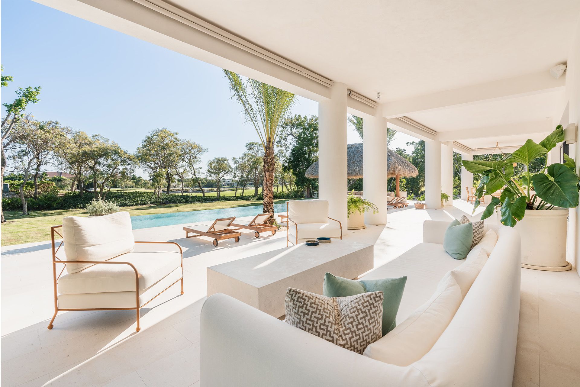 Bright white patio lounge with sofa, chairs, and pool view in a sunny tropical setting