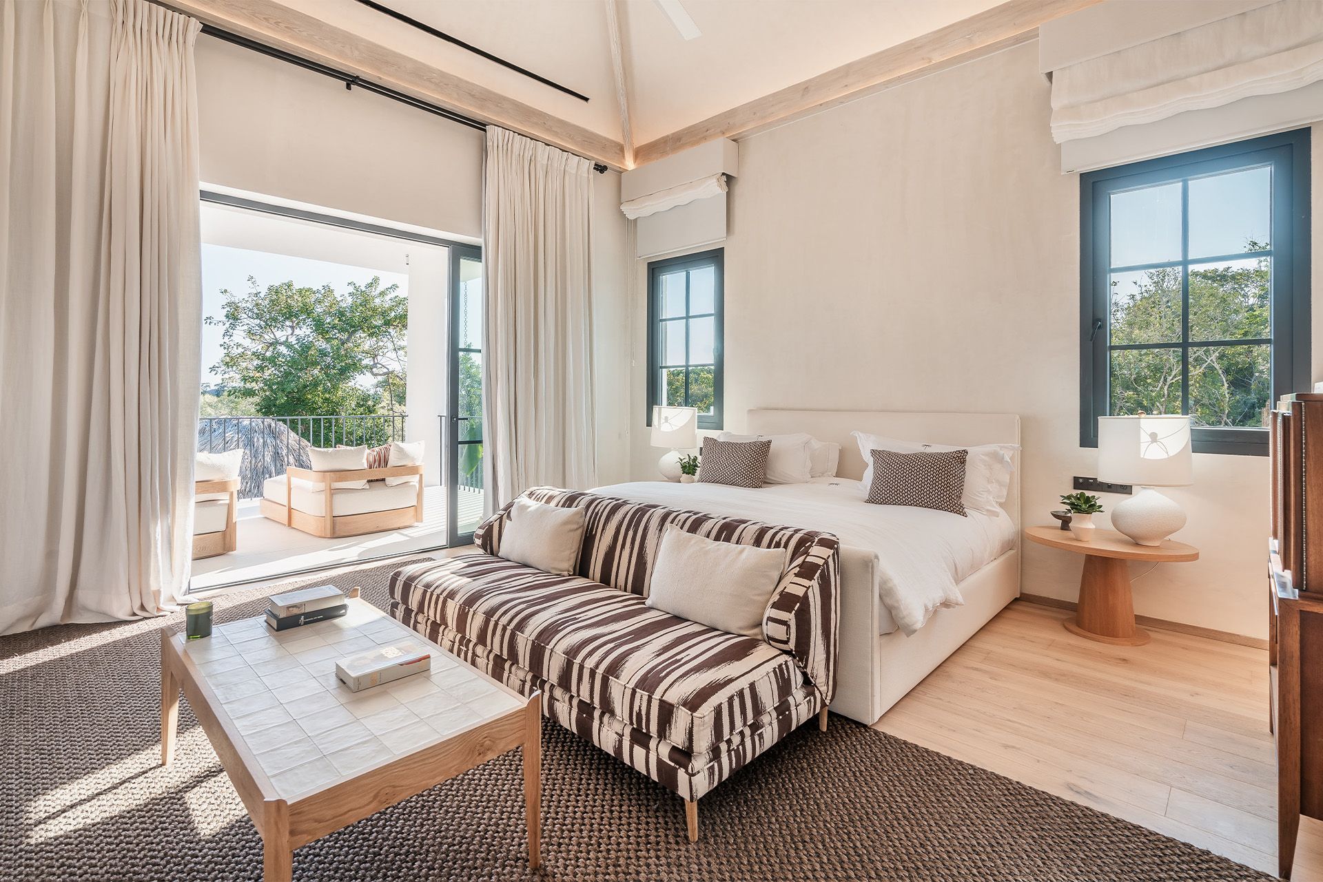 Bright bedroom with a zebra-print sofa, white bed, natural light, and a balcony view